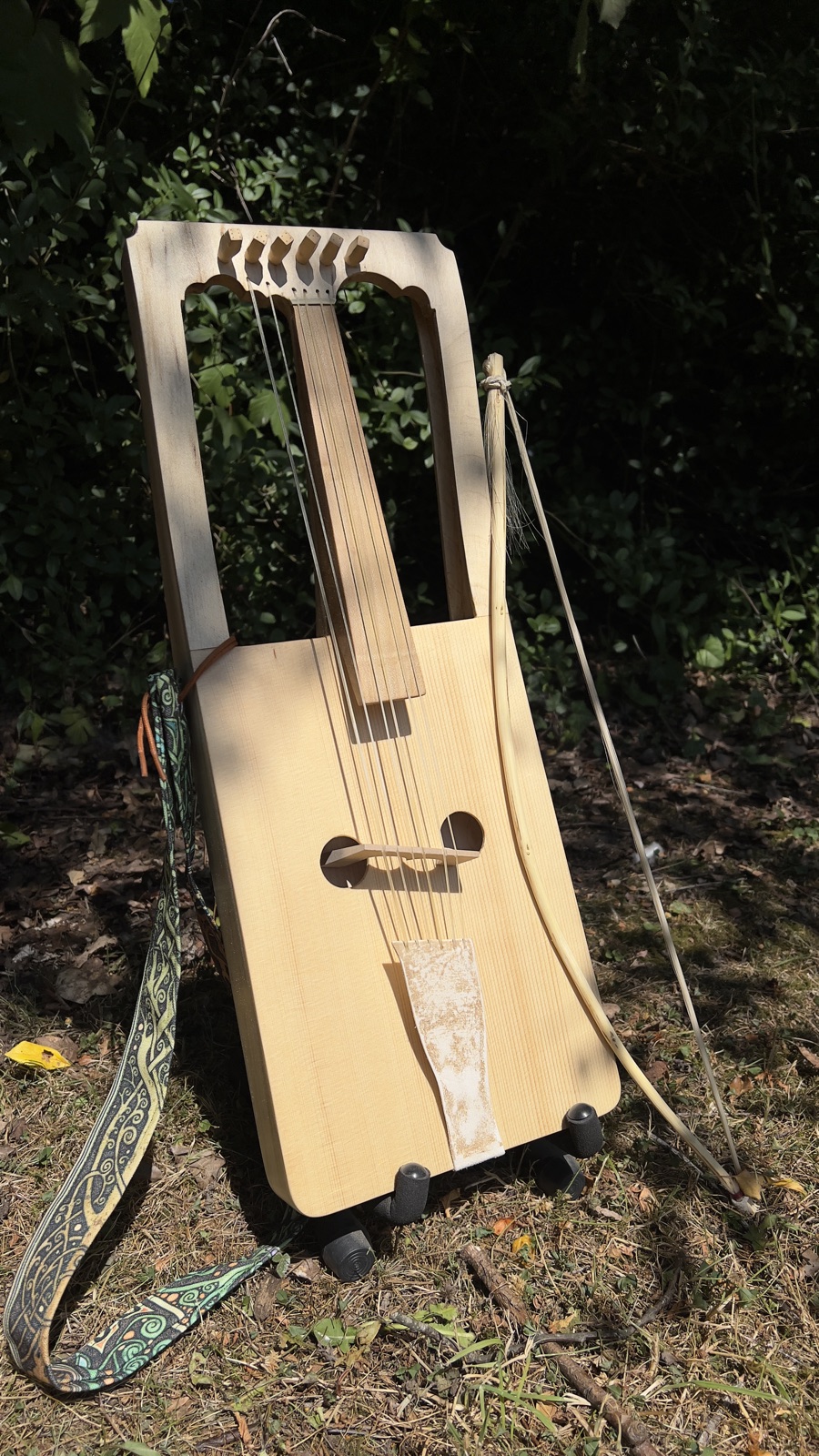A finished crwth on a stand in the garden, its bow beside it