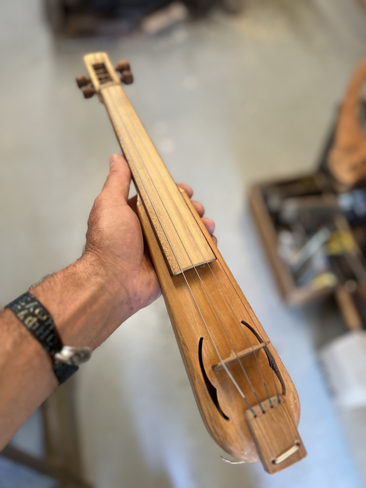 A small carved dance-fiddle held in the hand — the body cut from a single block, with two soundholes and four strings