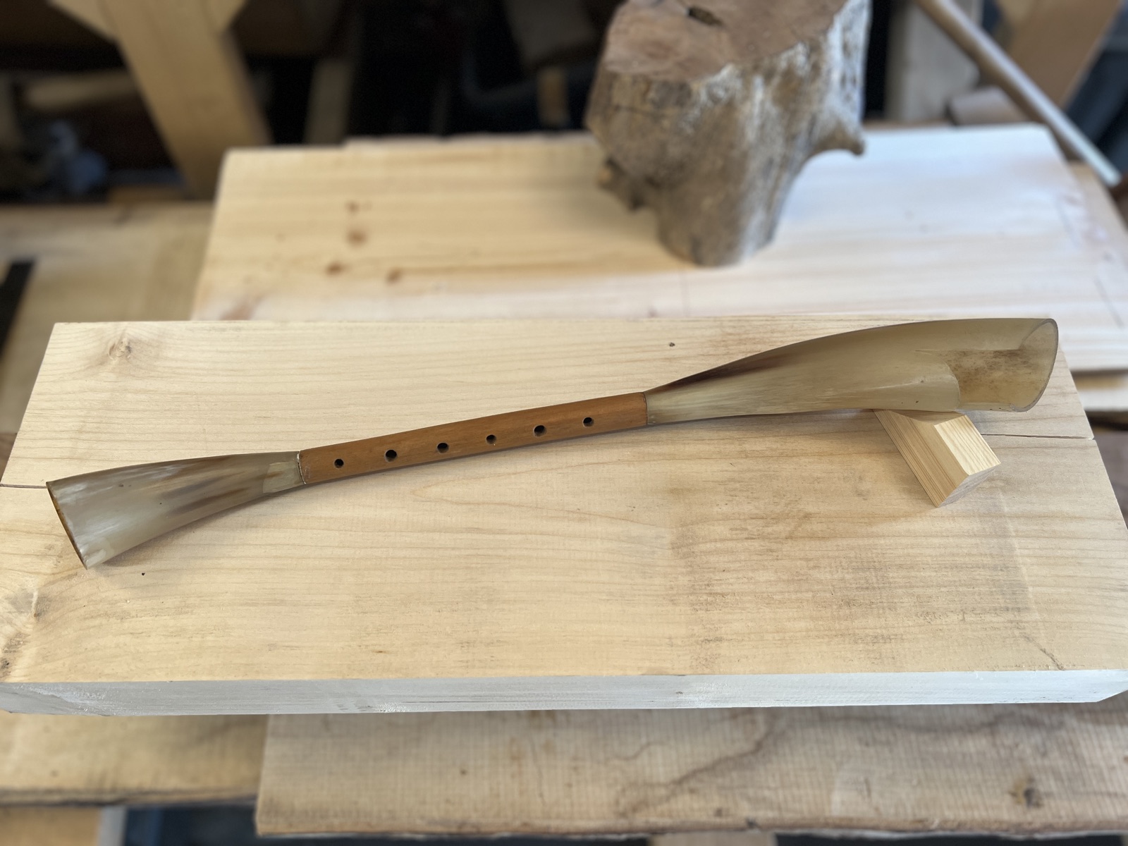 A finished pibgorn on the bench — an elder pipe with a cow-horn mouthpiece at one end and a flared horn bell at the other
