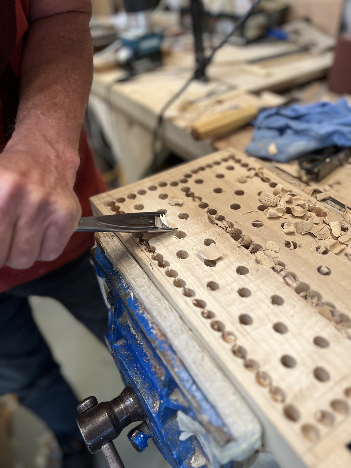 A gouge carving the waste from a crwth body drilled full of depth-holes, clamped in the vice
